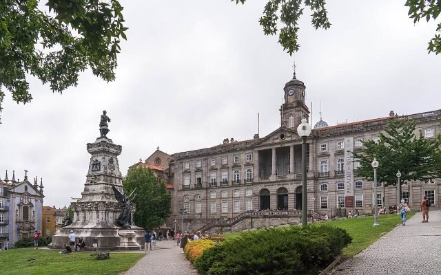 The neoclassical façade of the Palácio da Bolsa behind a garden and statue