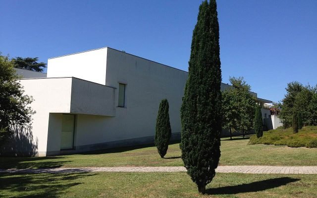 The white modernist building of the Serralves museum beside a lawn and cypress tree