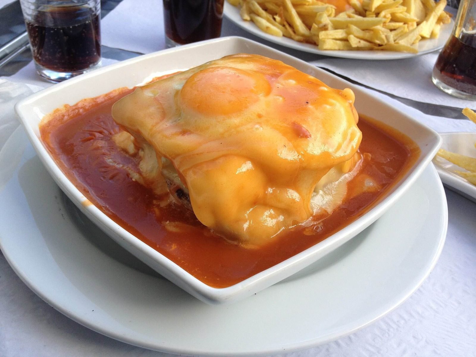 A francesinha sandwich topped with a fried egg in a bowl of sauce