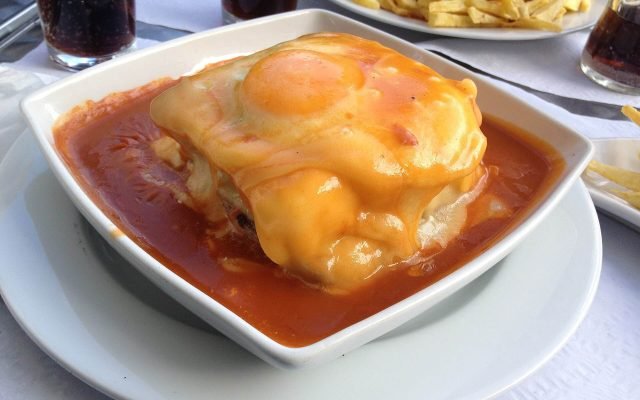 A francesinha sandwich topped with a fried egg in a bowl of sauce
